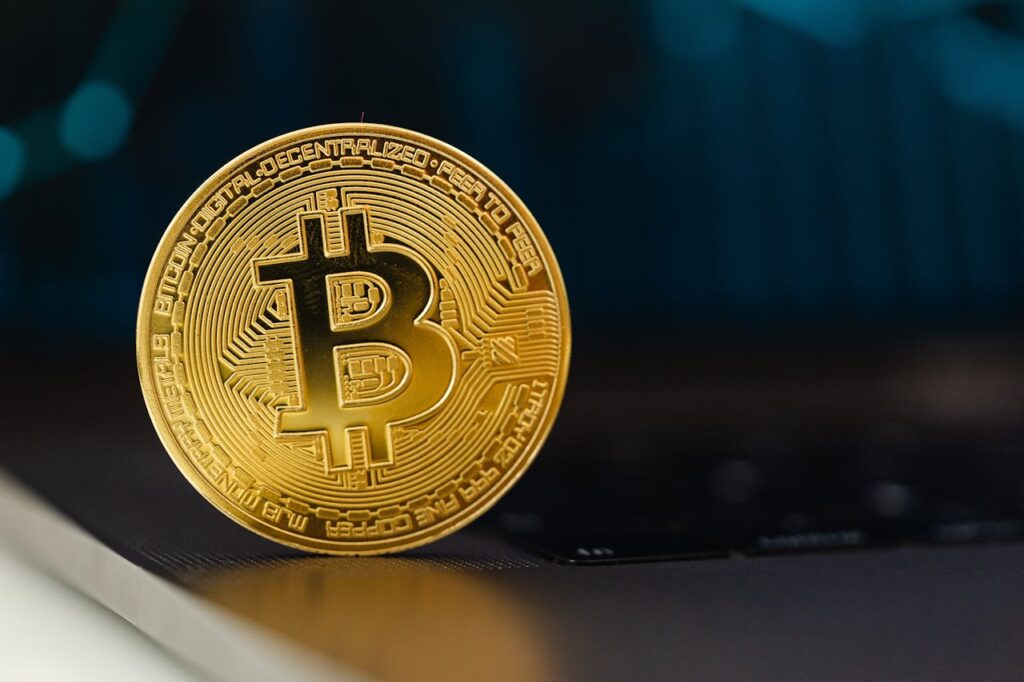 Golden Bitcoin coin standing upright on a laptop keyboard, representing digital currency.