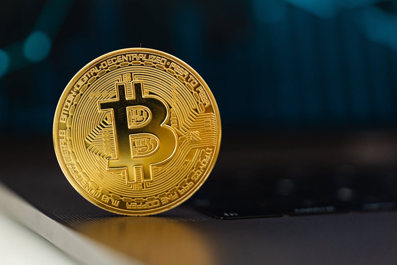 Golden Bitcoin coin standing upright on a laptop keyboard, representing digital currency.
